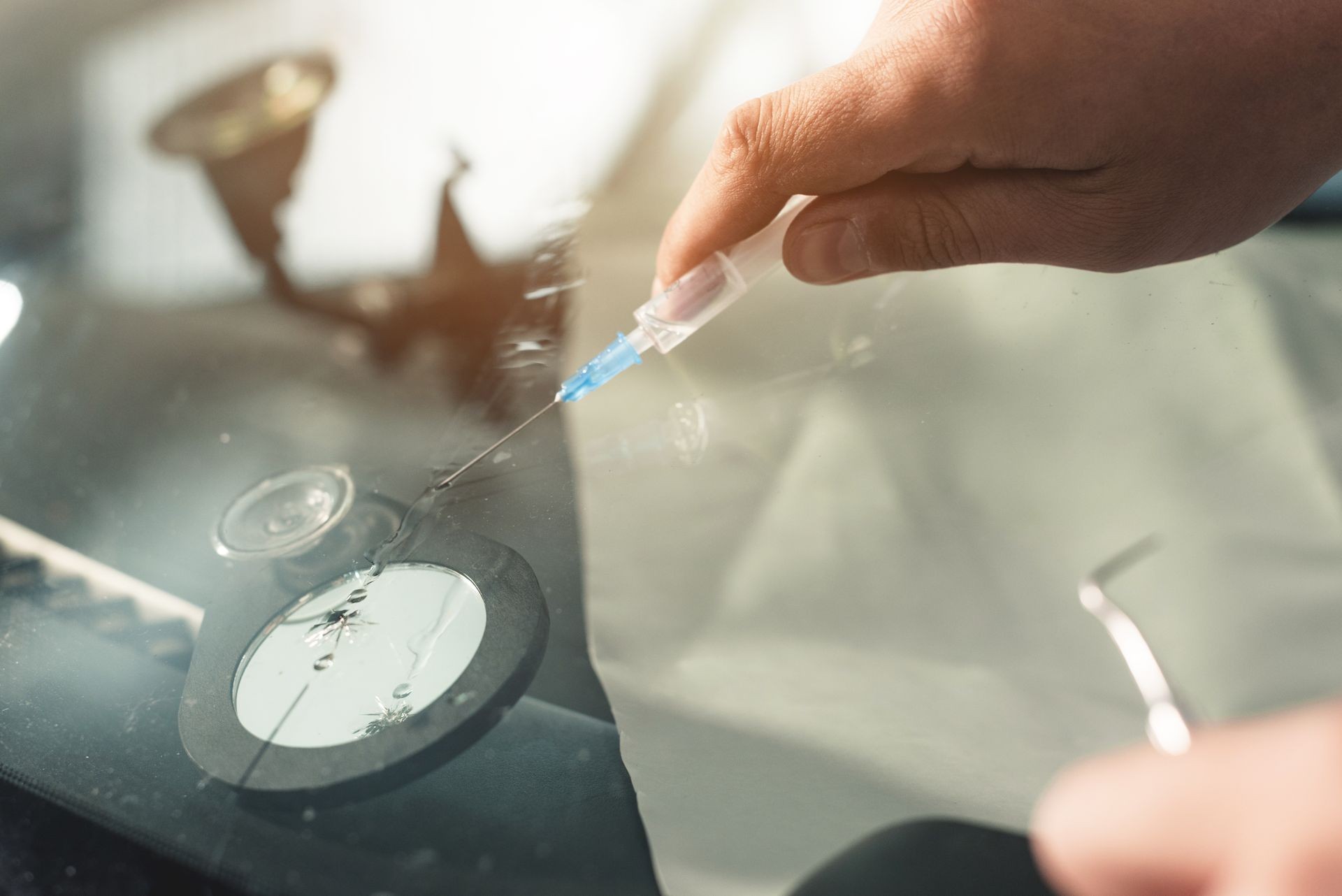 Close-up of a hands of professional windshield repairman fills a crack in the glass with a special polymer through a syringe. Elimination of cracks and chips on windshields Close-up of a hands of professional windshield repairman fills a crack in the glass with a special polymer through a syringe. Elimination of cracks and chips on windshields